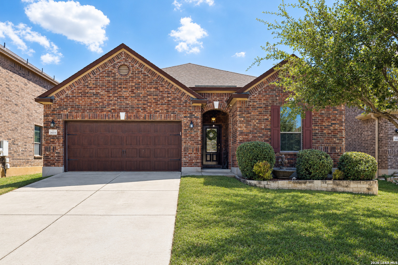 Red-brick home with a dark double garage, landscaped front yard, and concrete driveway.