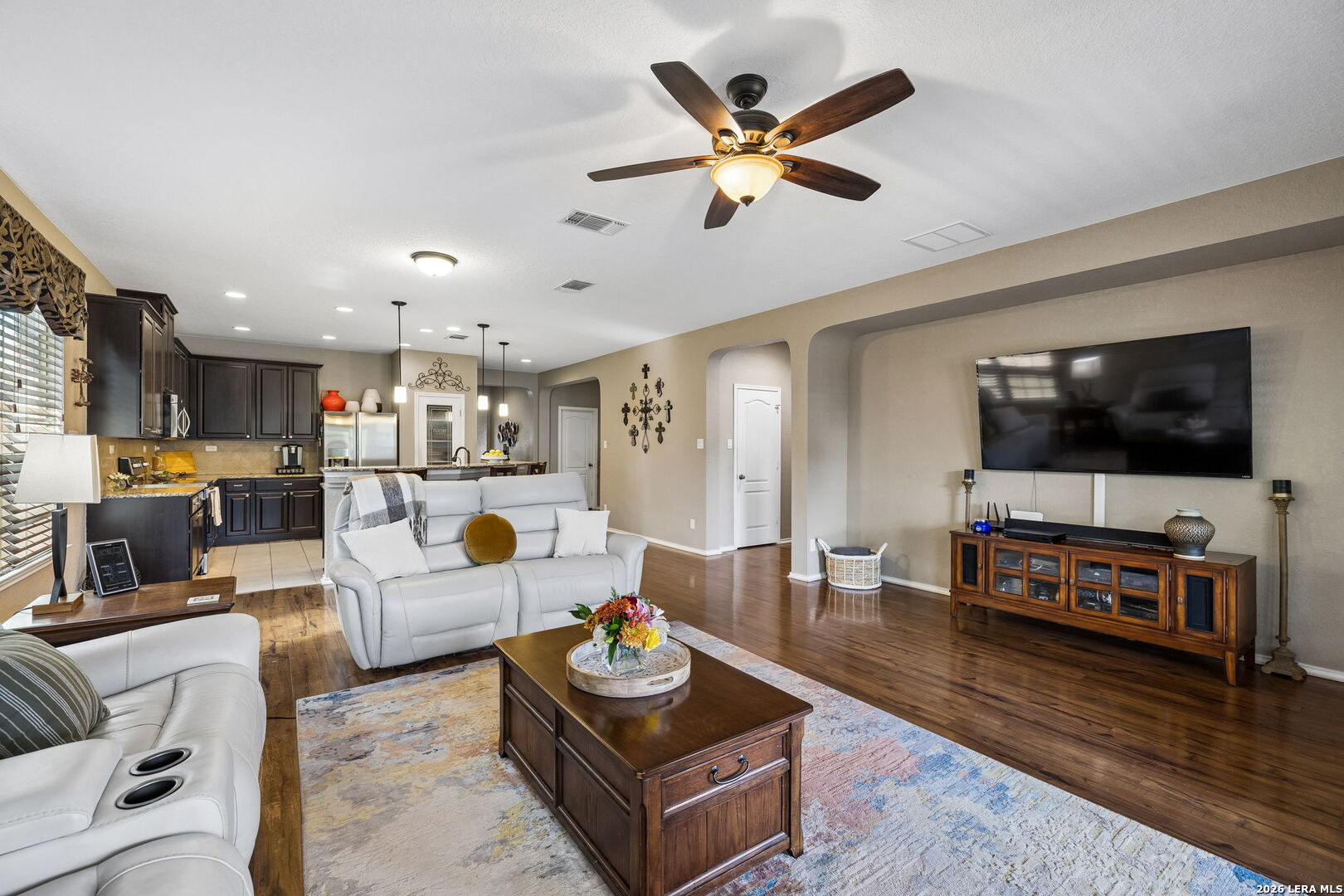 Open-plan living room with white sofas, hardwood floors, and a view into the dark-cabinet kitchen.