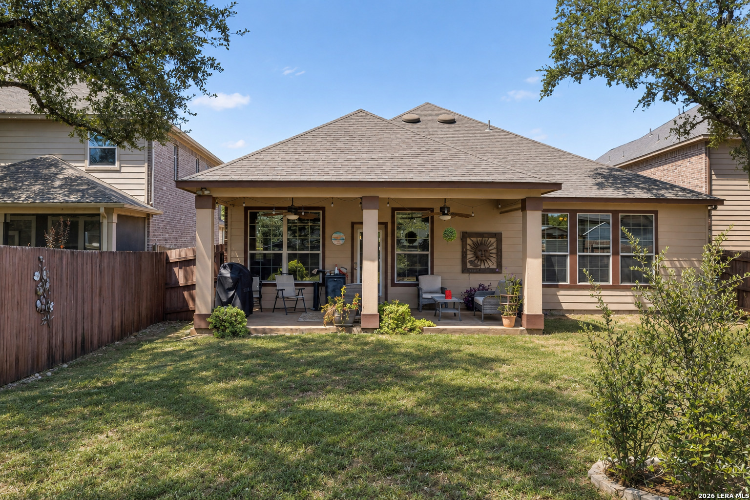 House rear exterior with covered patio, outdoor seating, lawn, and wooden privacy fence.