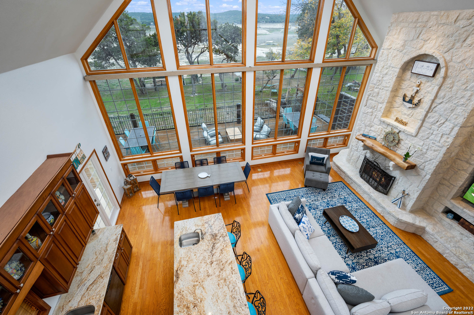 Open-plan living and dining room with soaring windows, a stone fireplace, and a water view.