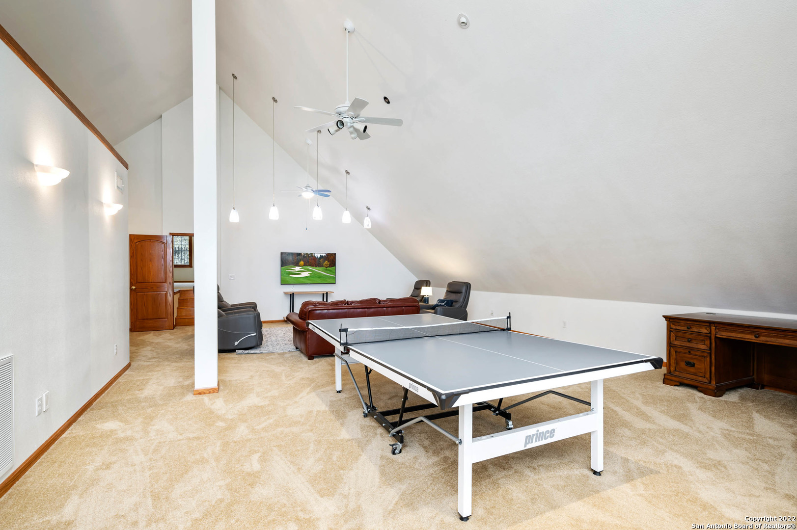 Upstairs game room with a ping-pong table and a seating area beneath a vaulted ceiling.