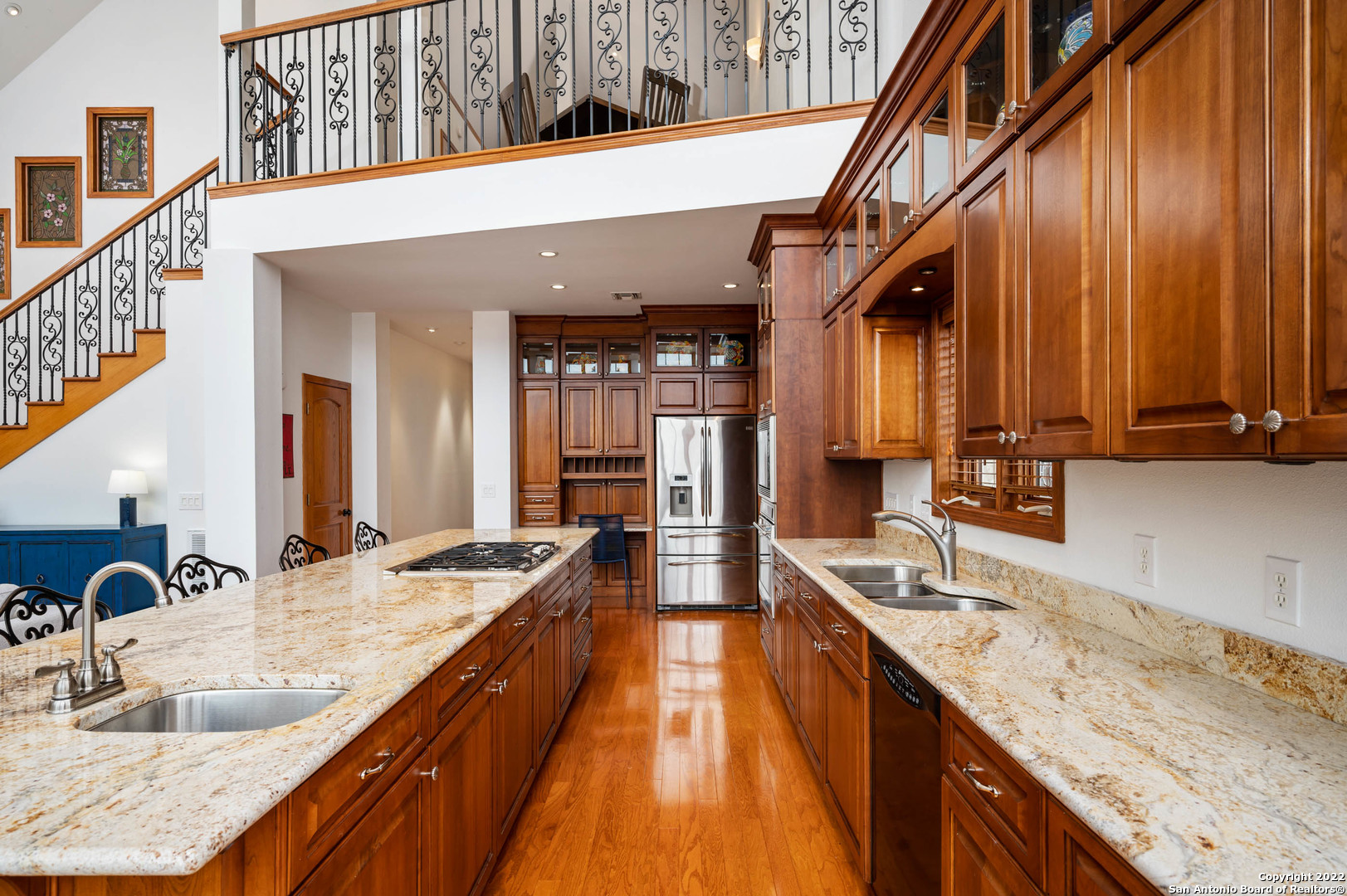 Kitchen with wood cabinetry, granite counters, a large island, stainless steel appliances, and an ornate staircase.