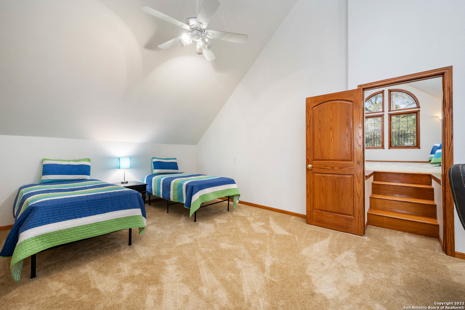 Bedroom with two striped twin beds and an open doorway leading to a landing with arched windows.