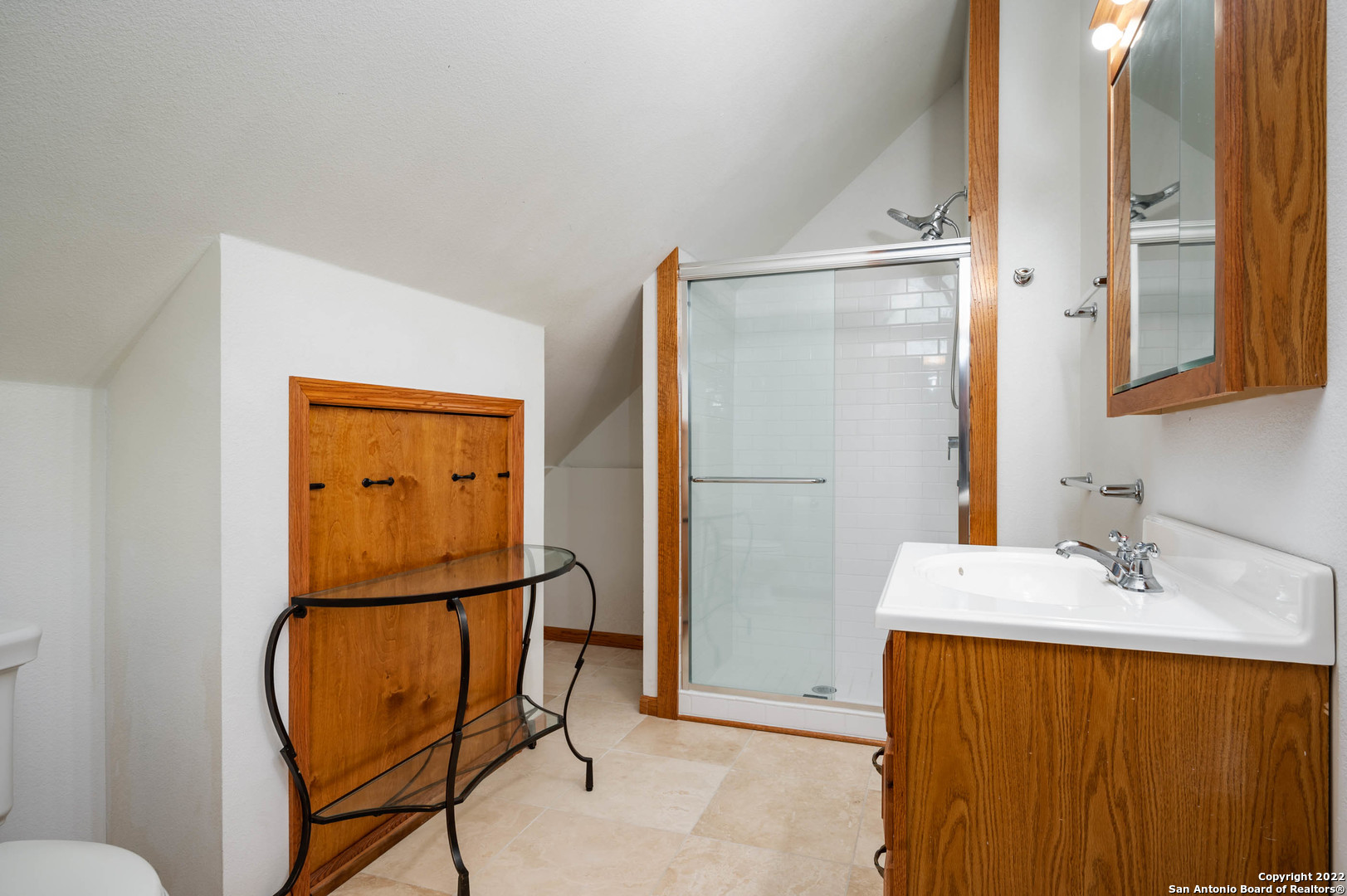 Bathroom with glass subway-tile shower, wood vanity, mirrored cabinet, and sloped ceiling.