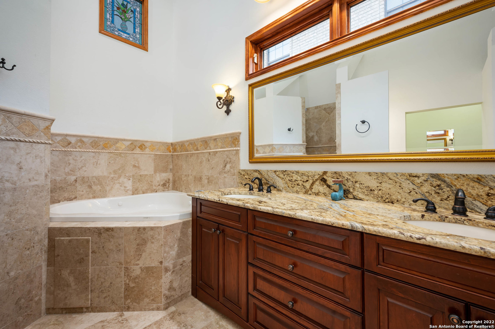 Bathroom with a tiled corner soaking tub, granite vanity, oversized mirror, and clerestory windows.