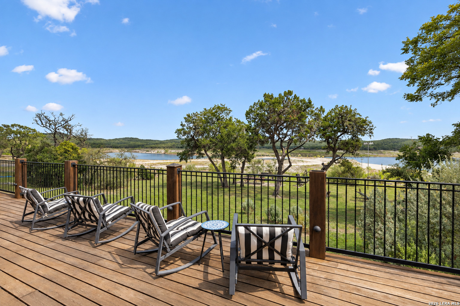 Furnished deck with striped lounge chairs overlooking a lake and tree-covered hills.