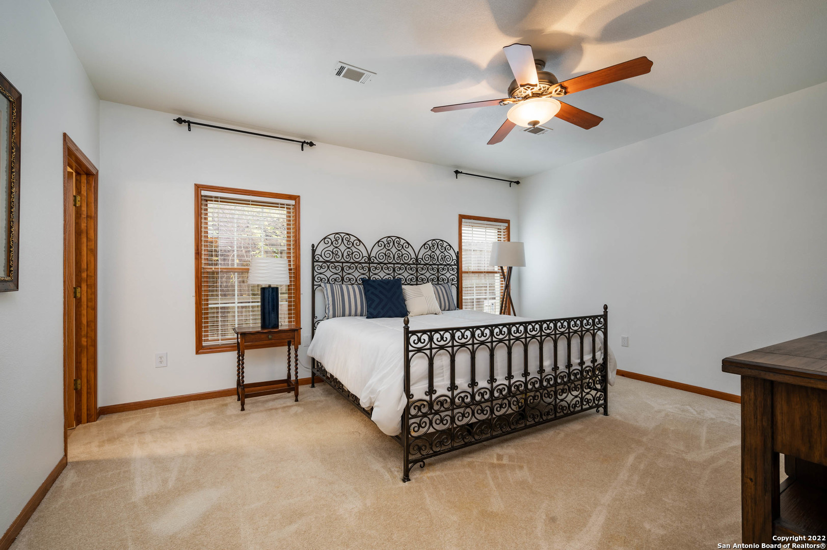Bedroom with an ornate wrought-iron bed, blue accent pillows, and wooden window trim.