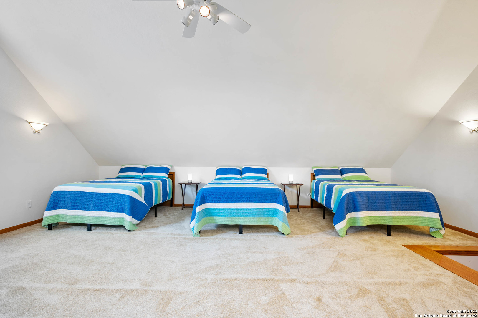 Bedroom with three side-by-side beds in blue, turquoise, white, and green striped bedding.