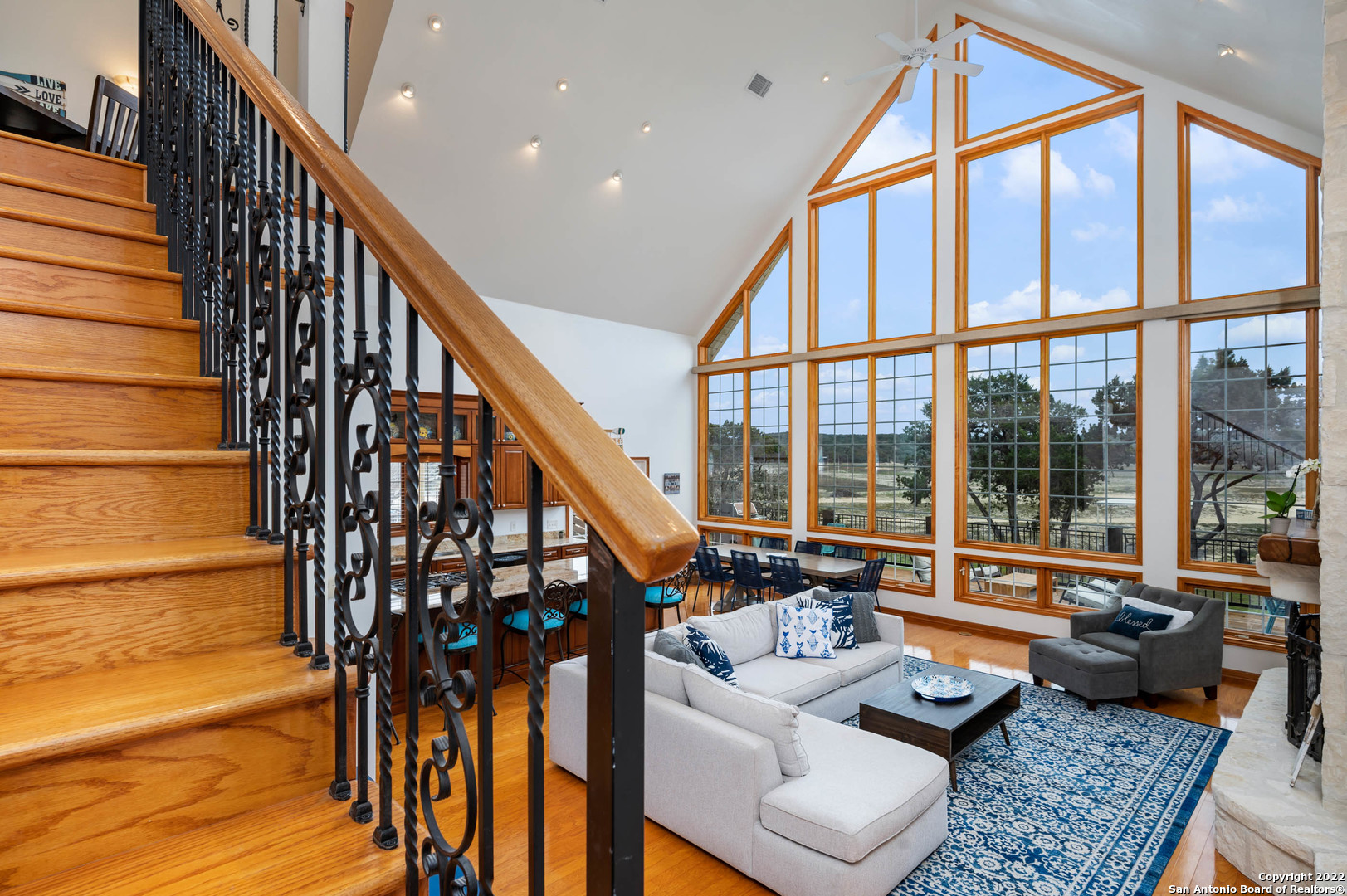 Two-story living room with a sweeping wooden staircase, towering windows, and a white sectional on a blue rug.