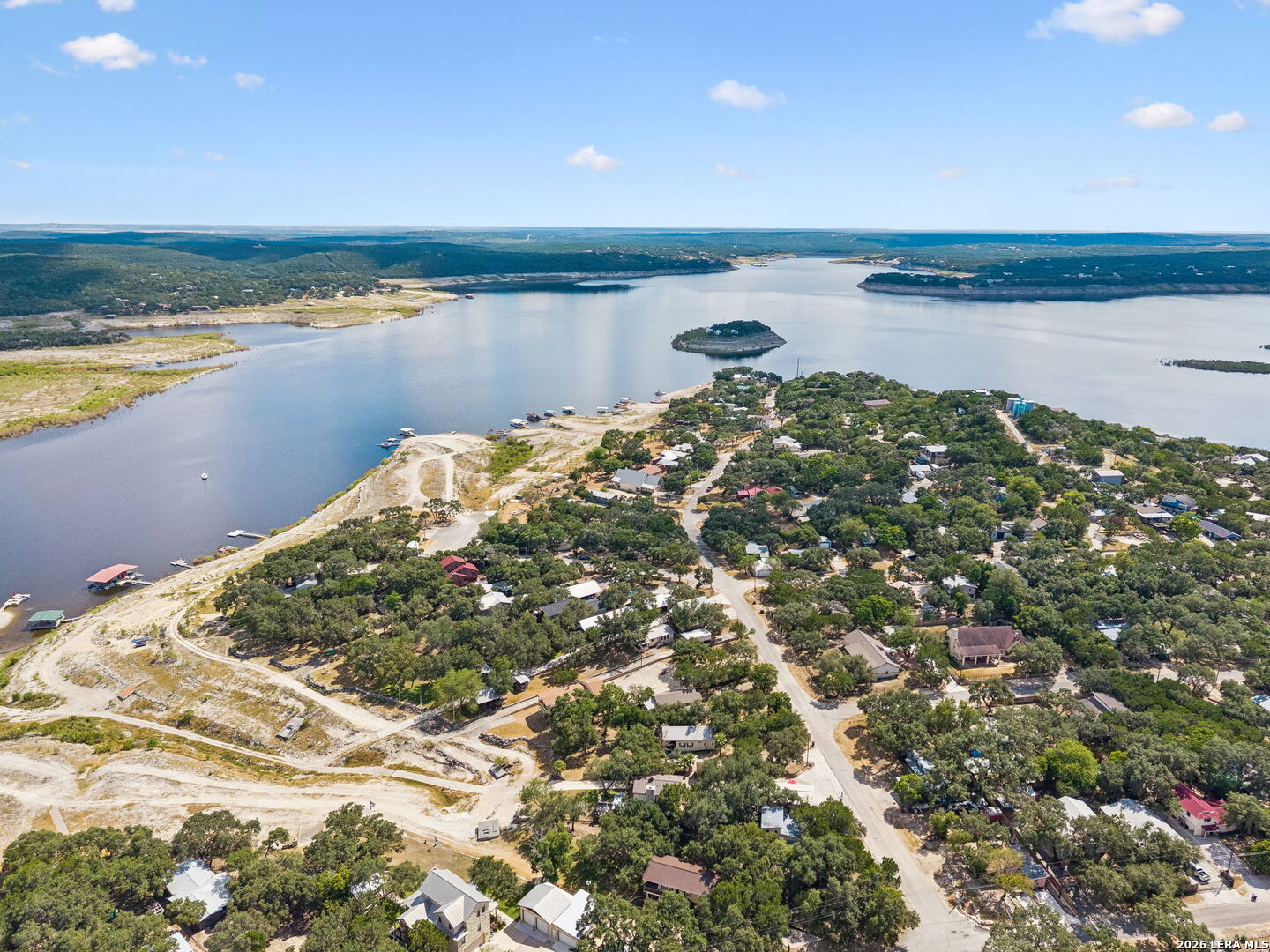 Aerial view of lakeside homes among trees, with docks and a small island in the lake.