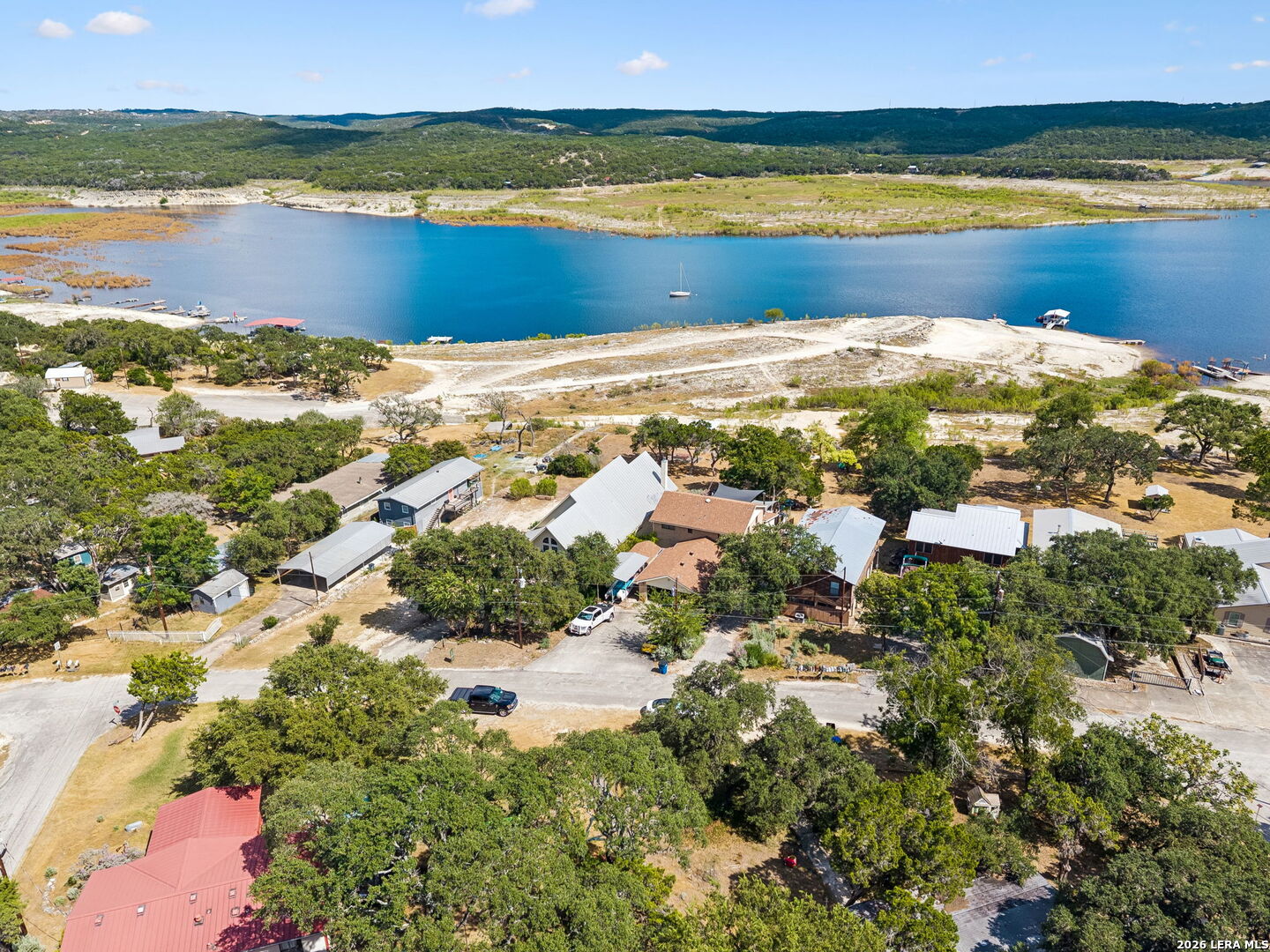 Aerial view of lakeside homes and docks beside a blue lake, with wooded hills beyond.