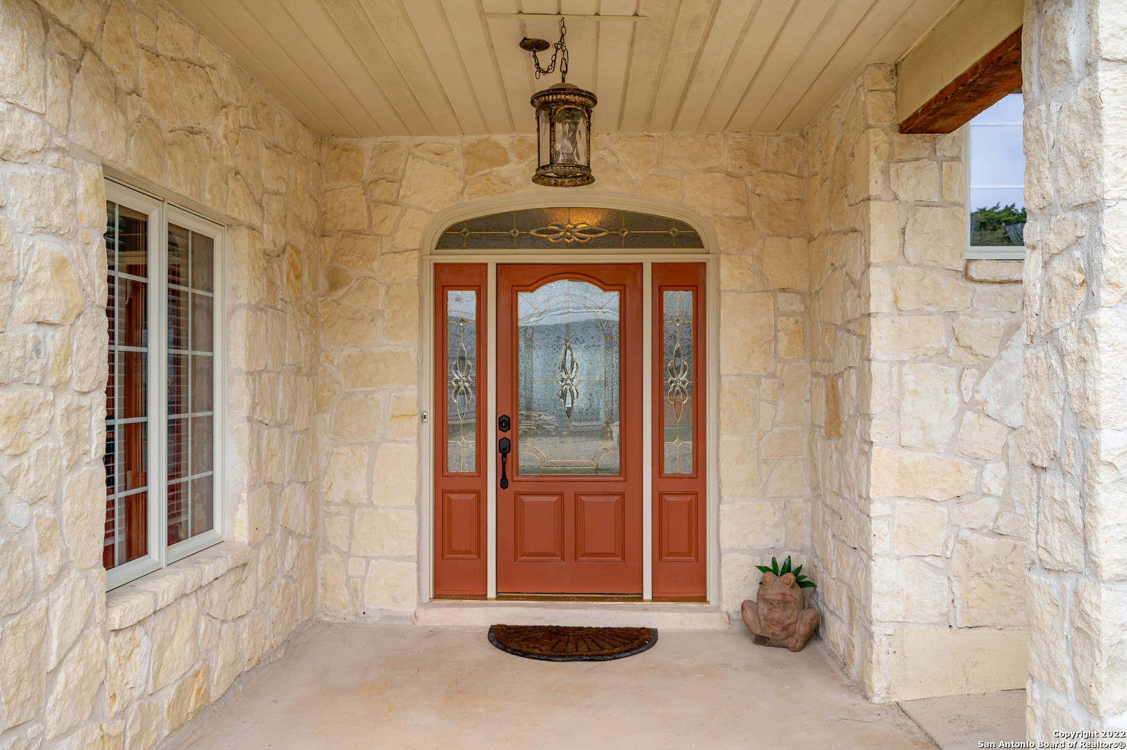 Stone-covered entry with a reddish-brown decorative glass front door and hanging lantern.