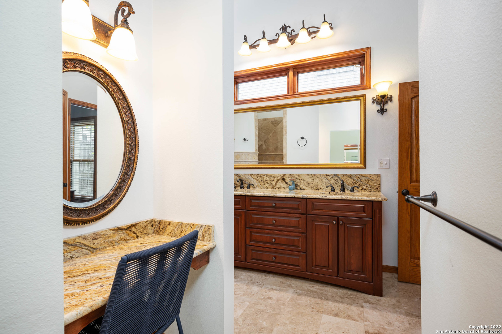 Bathroom with twin granite vanities, dark wood cabinets, ornate mirrors, and bronze lighting.