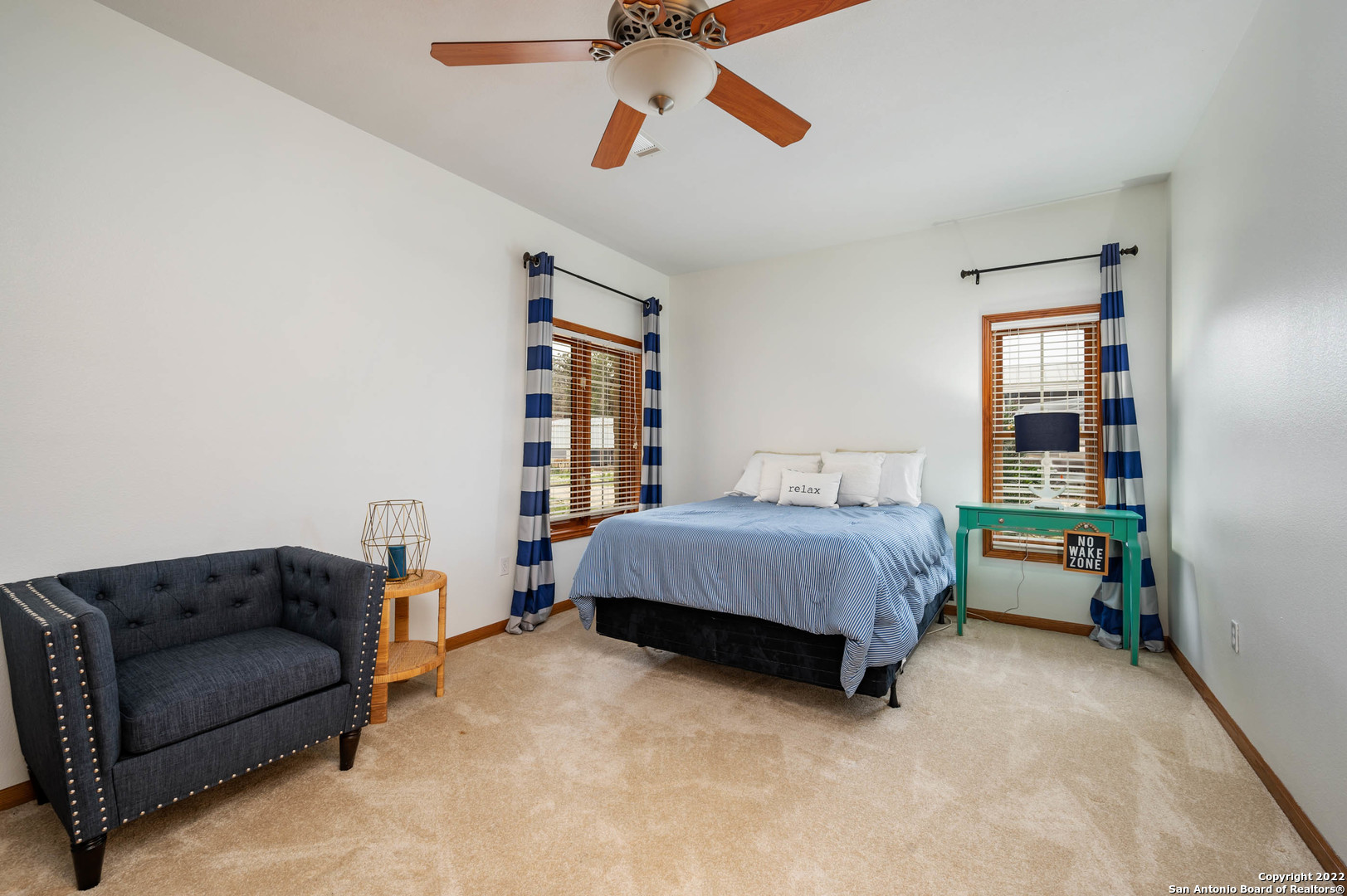 Furnished bedroom with a striped bed, teal console table, and dark tufted armchair.