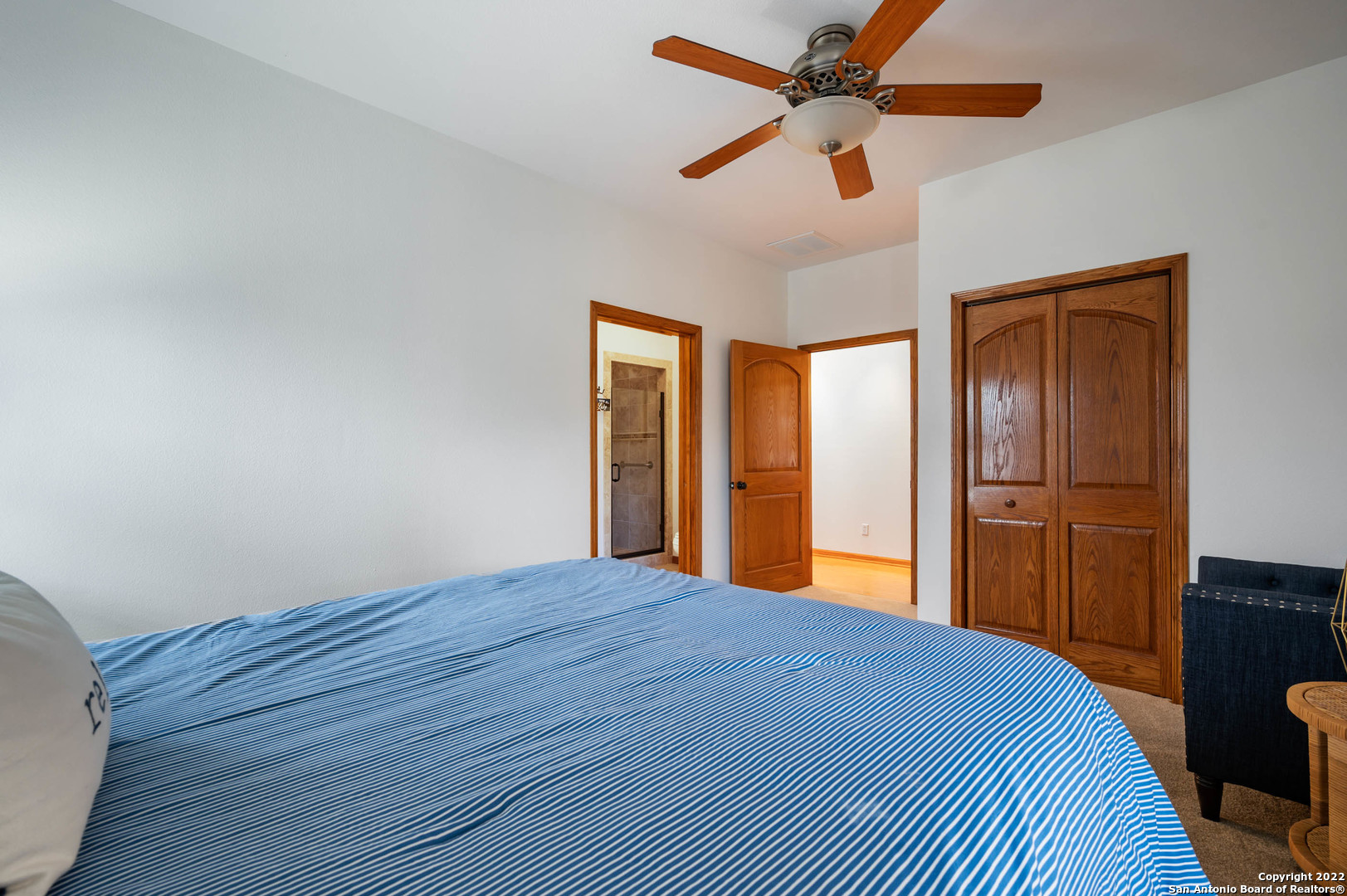 Bedroom with a blue-and-white striped bedspread, wood doors and trim, and a ceiling fan.