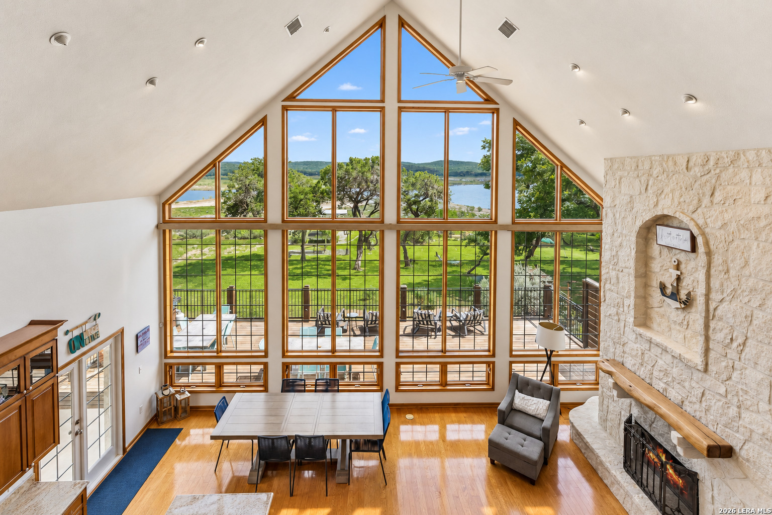 Furnished great room with soaring windows overlooking a lake and a stone fireplace.