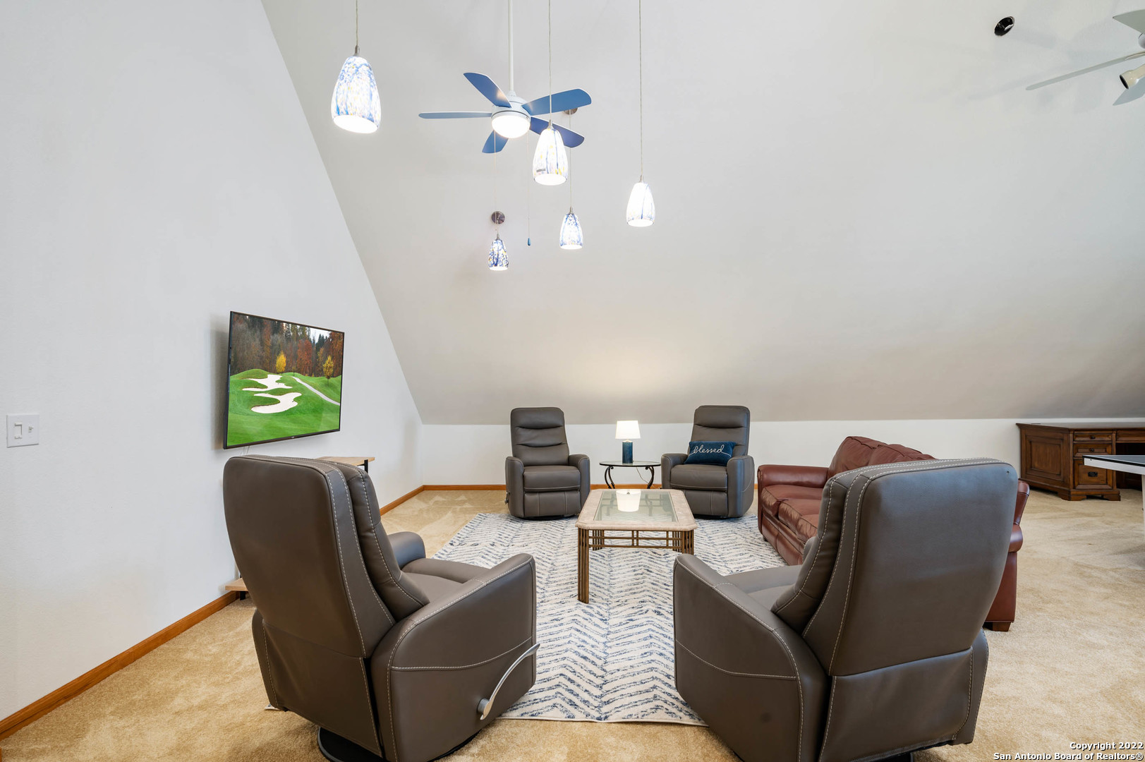 Furnished sitting room with leather recliners, a patterned rug, pendant lights, and a high sloped ceiling.