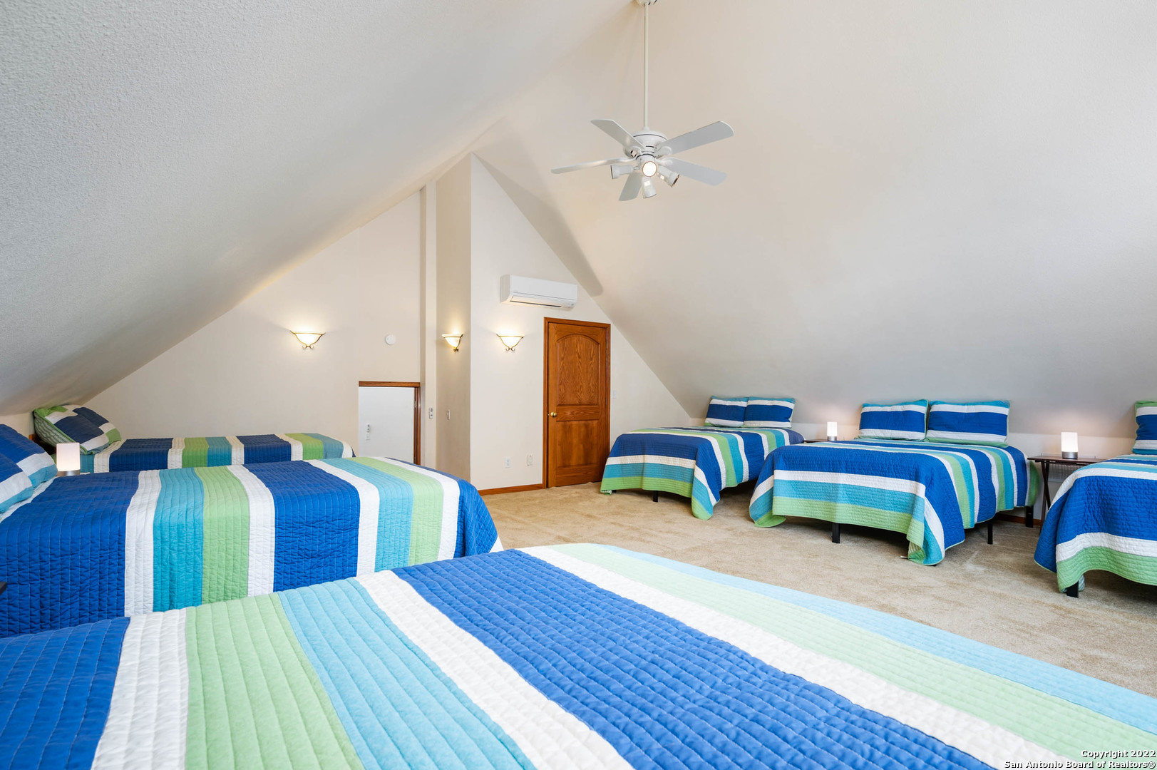 Loft bedroom with several beds in matching blue, turquoise, green, and white striped quilts.