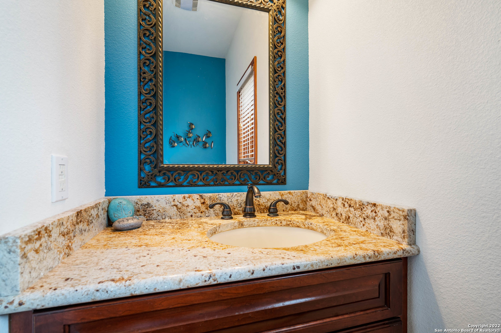 Bathroom vanity with a mottled stone countertop, ornate mirror, and vivid blue accent wall.