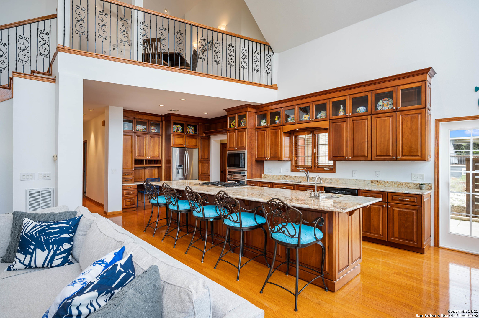 Kitchen with a long granite island, turquoise bar stools, rich wood cabinetry, and an open upper-level landing.