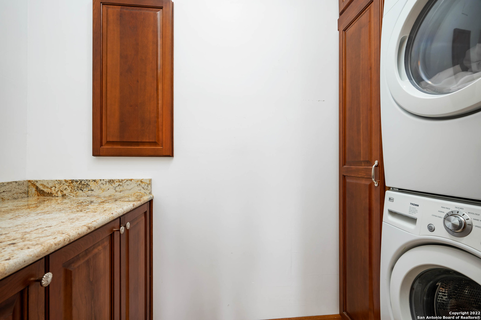 Laundry room with stacked front-load washer and dryer beside wood cabinetry and a granite counter.