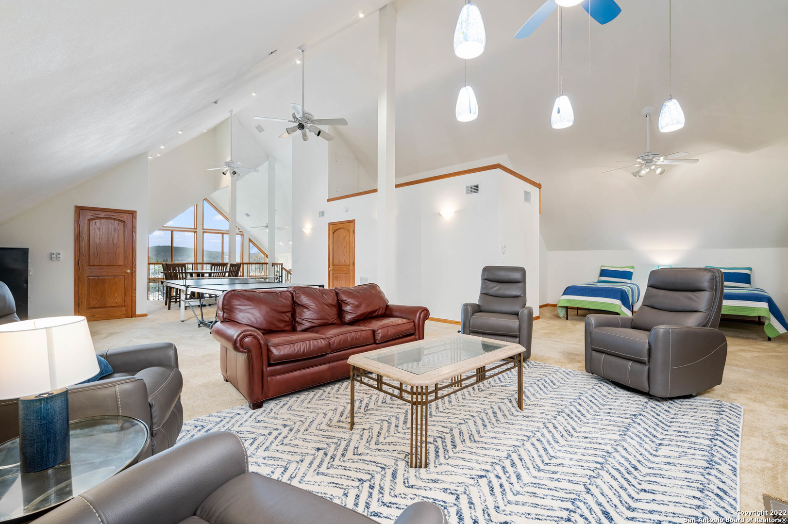 Vaulted living area with leather seating, two beds, and a ping-pong table by large windows.