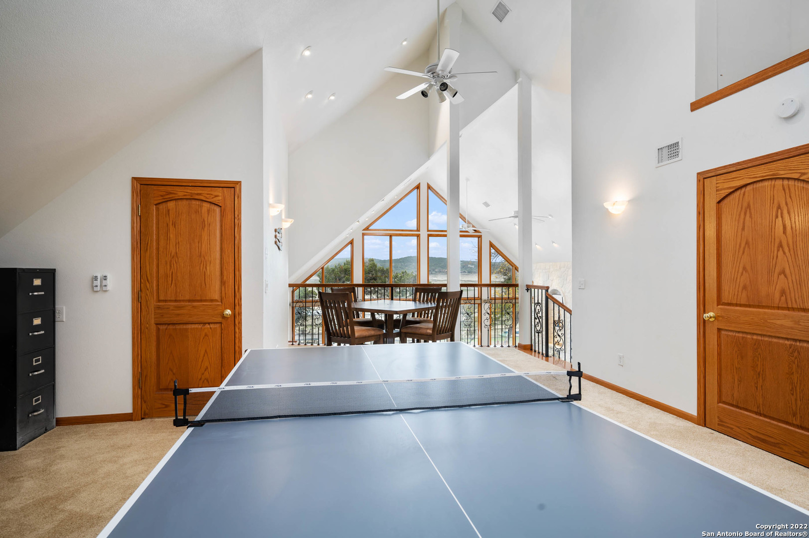 Vaulted game room with a ping-pong table and lake views through tall triangular windows.