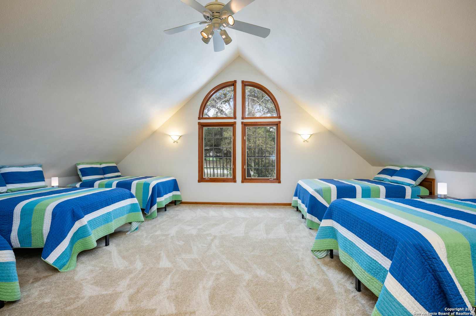 Furnished bedroom with four striped beds, a vaulted ceiling, and paired arched windows.