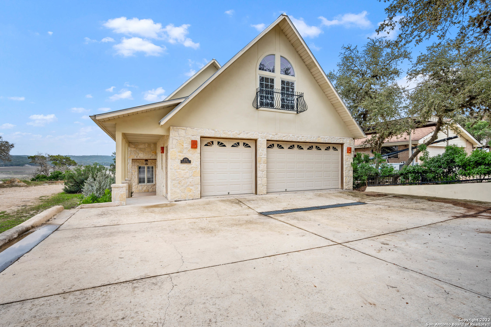 Gabled stone home with two garage doors, an upper balcony, and a broad concrete driveway.