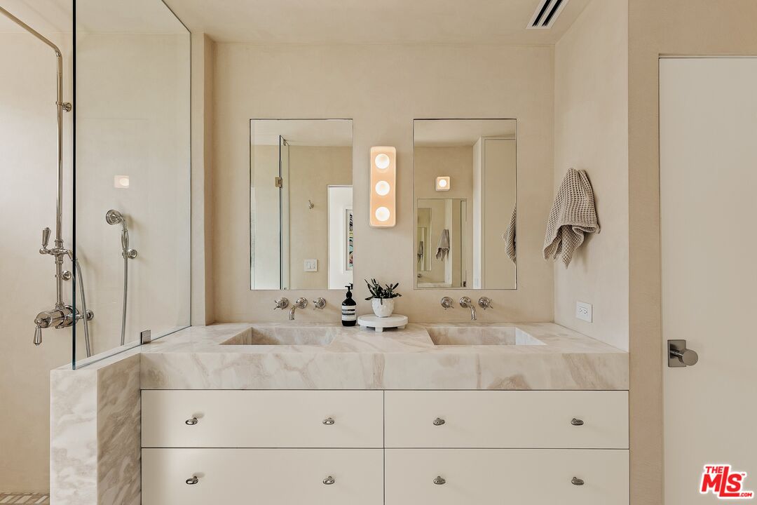 Bathroom with a marble double-sink vanity, twin mirrors, and a glass-enclosed shower.