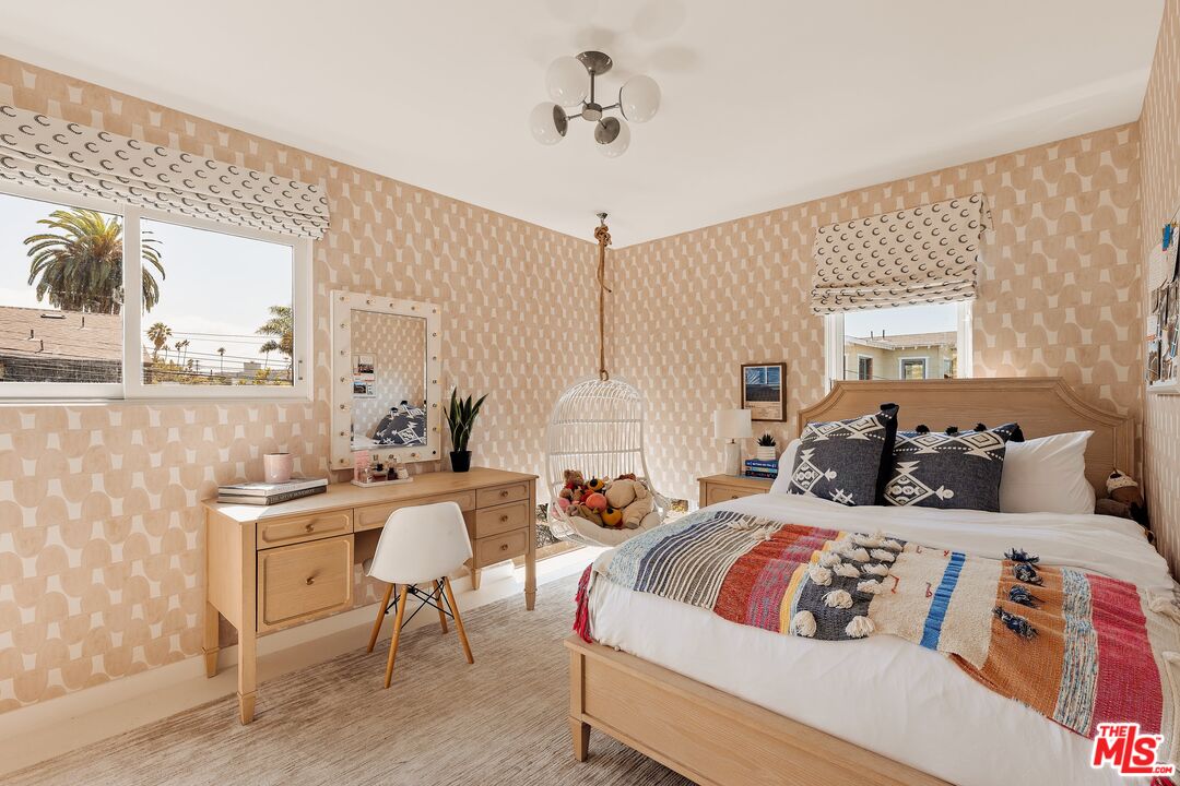 Bedroom with patterned wallpaper, a wooden bed, desk, and hanging basket swing