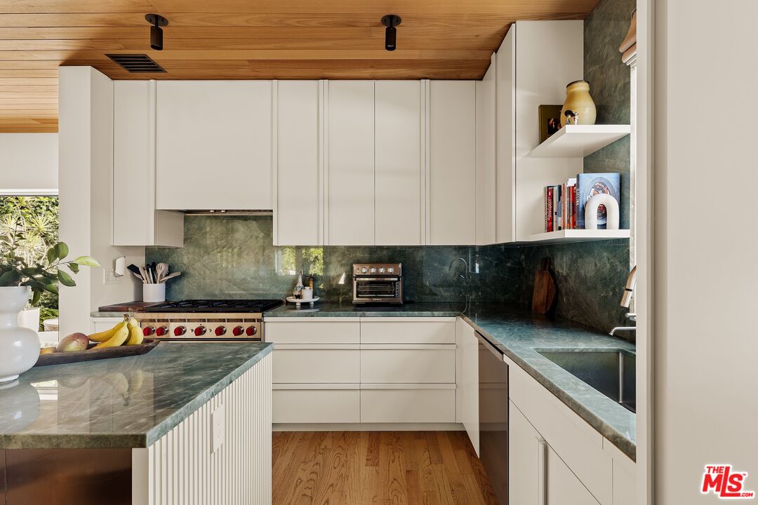 Modern kitchen with green stone counters, white cabinetry, and a warm wood ceiling.