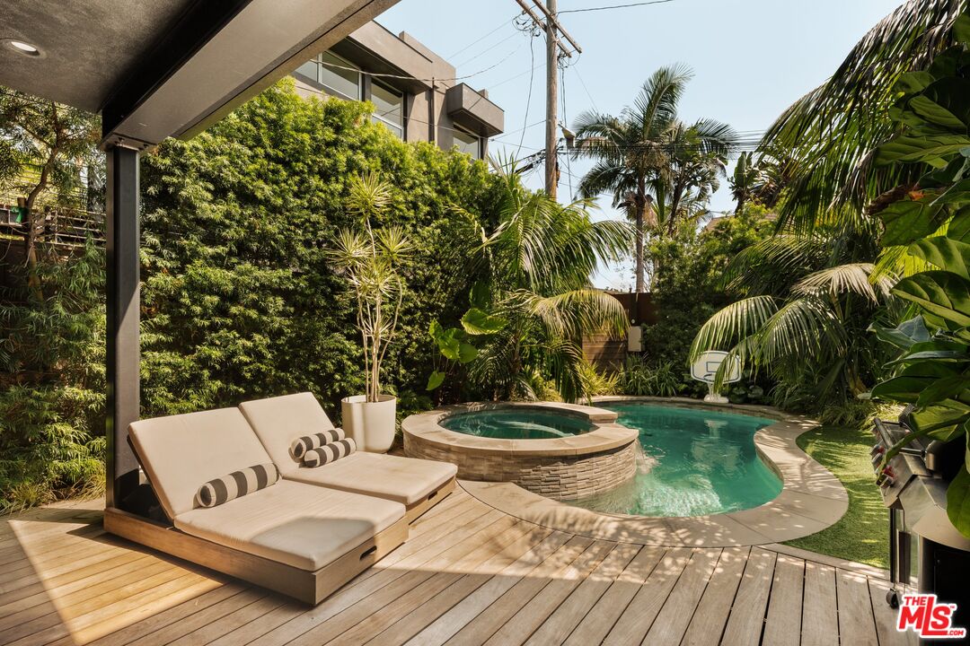 Backyard pool and raised circular spa beside a wooden deck with cushioned chaise lounges.