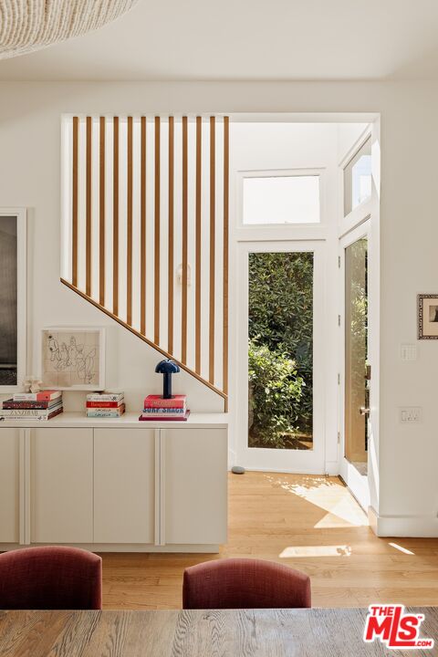 Bright entryway with a glass front door, leafy view, and wood-slat staircase divider.