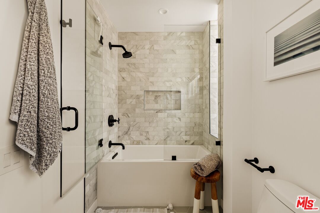 Bathroom with a marble-tiled tub and shower, glass enclosure, and matte black fixtures.