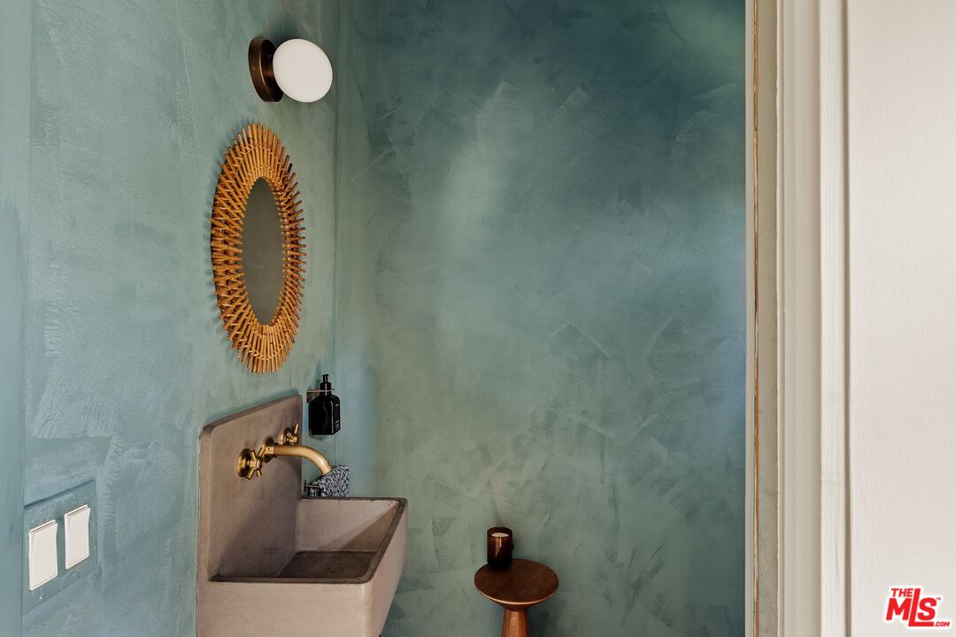 Bathroom sink with brass faucet, woven oval mirror, and textured teal walls.