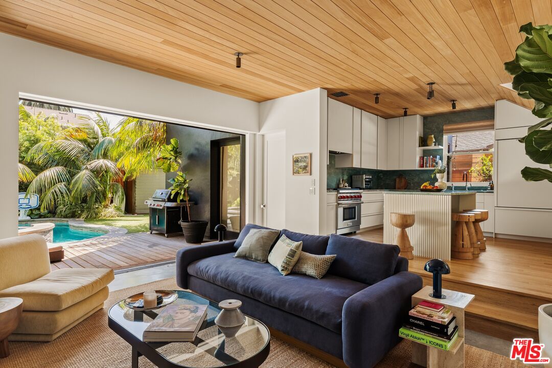 Open-plan living room and kitchen with a wood ceiling and sliding doors overlooking a backyard pool.