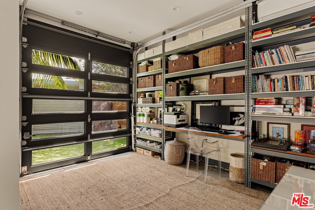 Organized garage office with a windowed black door, metal shelving, woven baskets, and a desk.