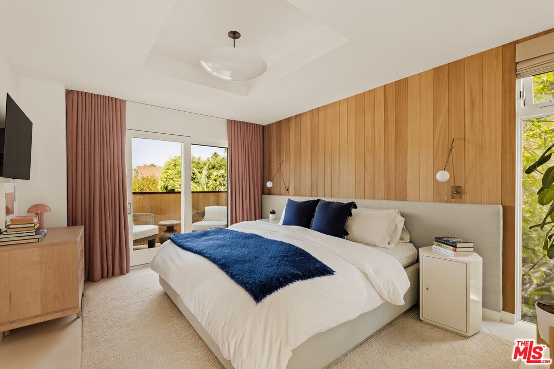 Bedroom with a wood-paneled accent wall, navy bedding accents, and glass doors opening to a balcony.