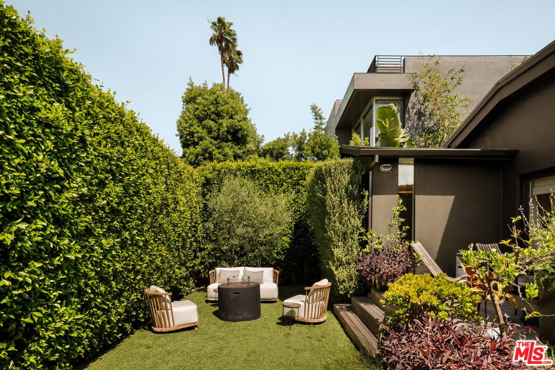 Backyard patio with lounge seating, artificial turf, tall privacy hedges, and a modern home exterior.