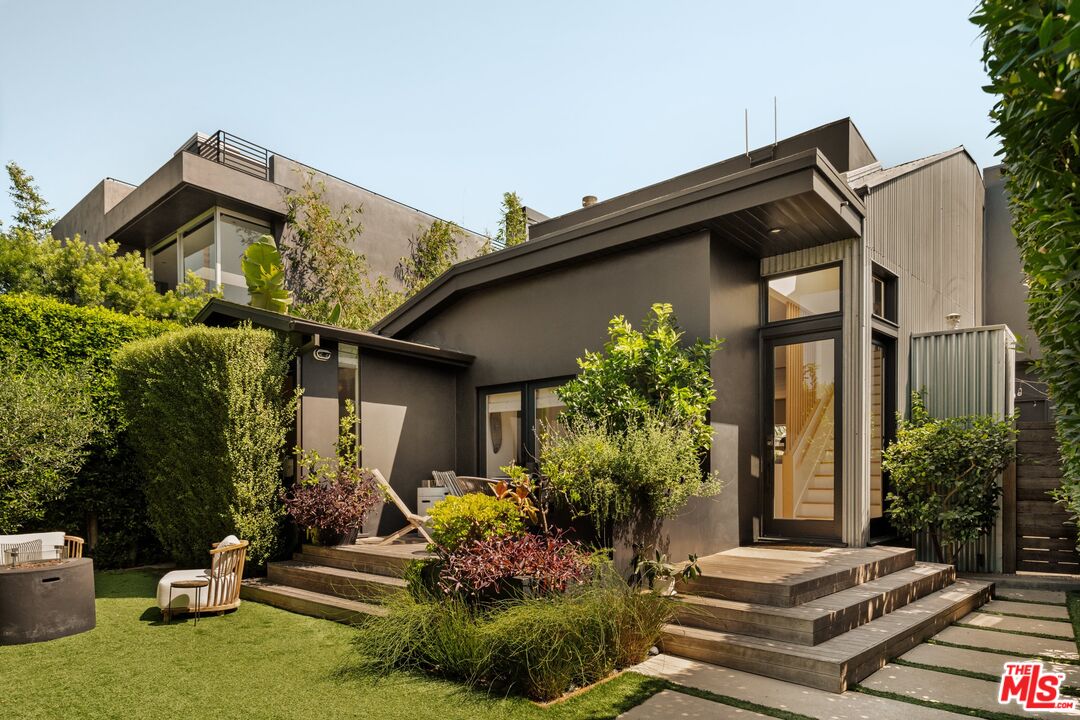Contemporary home with dark exterior, large windows, landscaped lawn, and broad patio steps.