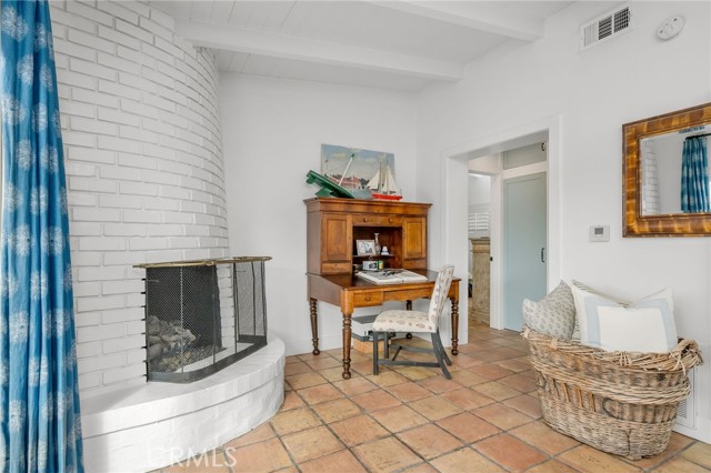 Sitting room with a curved white-brick fireplace, wooden writing desk, and wicker chair.
