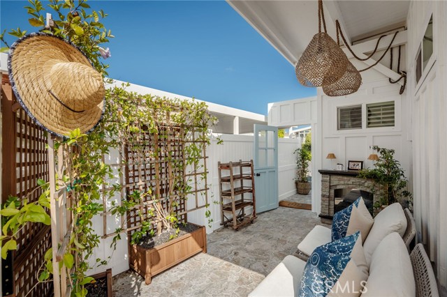 Outdoor patio with a brick fireplace, blue gate, lattice greenery, and white seating with patterned pillows.
