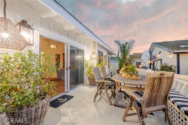 Furnished patio with a wooden dining set, potted palms, and sliding glass doors at dusk.
