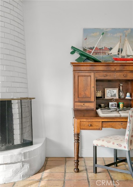 Furnished room with a wooden secretary desk, floral chair, and white brick fireplace.