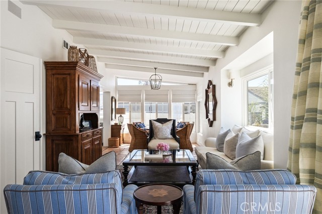 Living room with striped blue sofas, exposed white ceiling beams, and a dark wood cabinet.