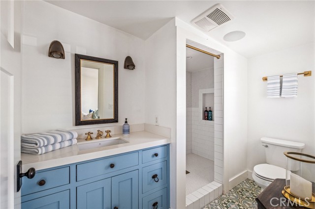 Bathroom with a blue paneled vanity, walk-in tiled shower, and patterned floor.