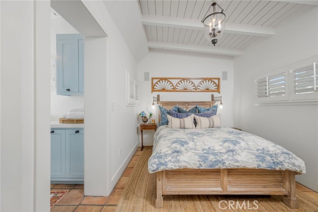 Bedroom with blue floral bedding, a wooden bed, exposed ceiling beams, and plantation shutters.