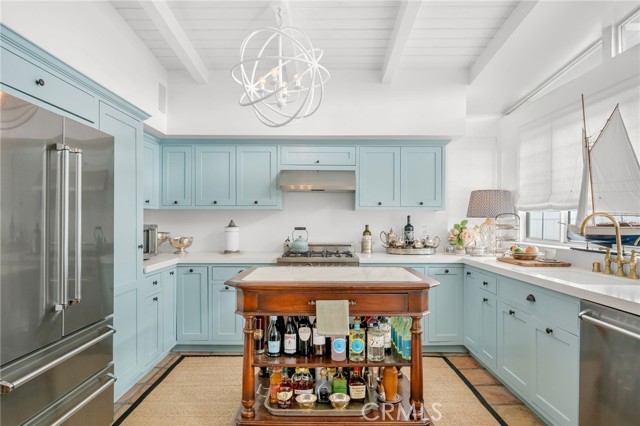 Kitchen with pale blue cabinets, stainless steel appliances, and a wooden island stocked with bottles and jars.