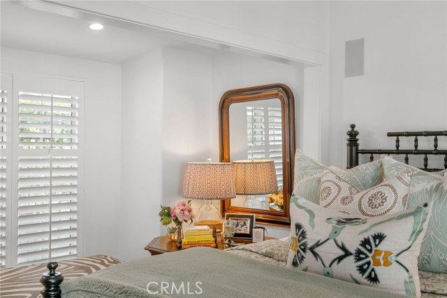 Bedroom with patterned pillows, a wood-framed mirror, and white plantation shutters.